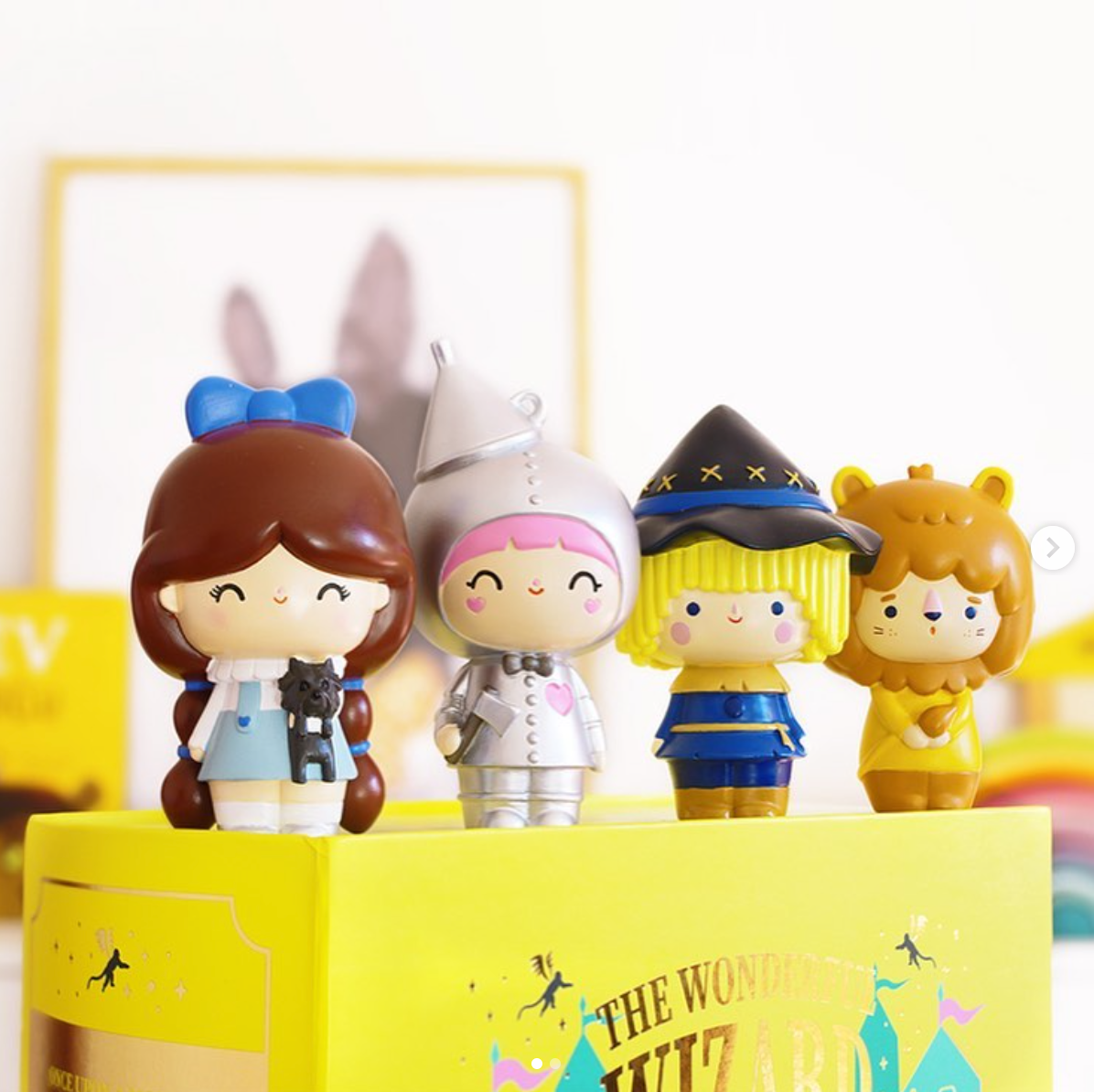 Four Momiji dolls from The Wonderful Wizard of Oz stand on a yellow book titled “The Wonderful Wizard.”. — Momiji doll