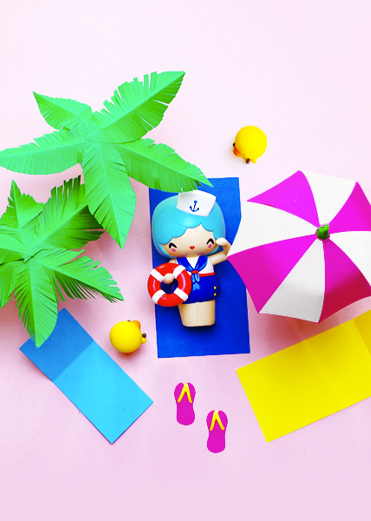 Marina Momiji doll sailor on a blue mat with paper palm trees, beach towels, flip-flops, and yellow balls. — Momiji doll