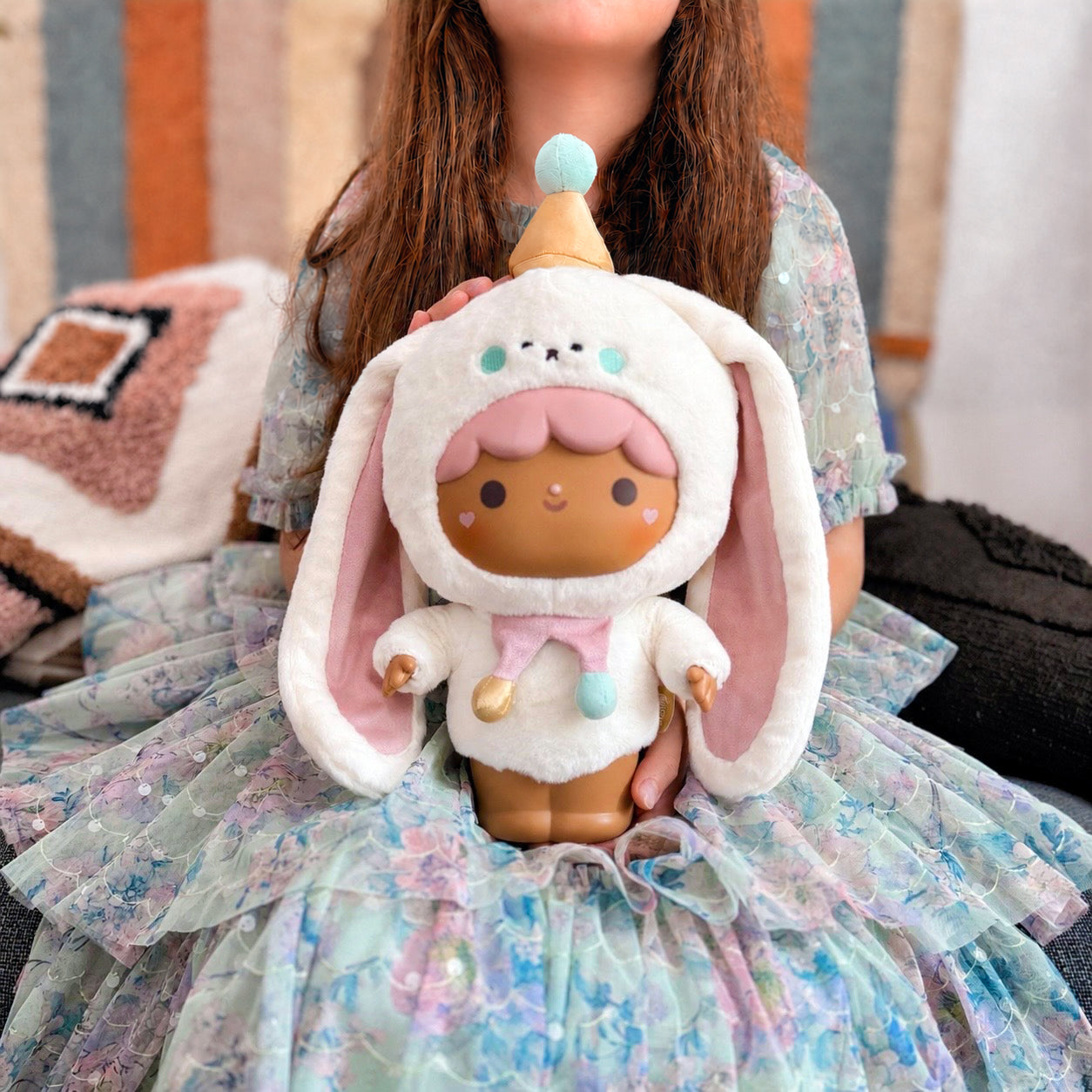A girl in a pastel dress holds the Bonbon Butterkins Momiji doll plush, featuring pink bunny ears and a party hat. — Momiji doll