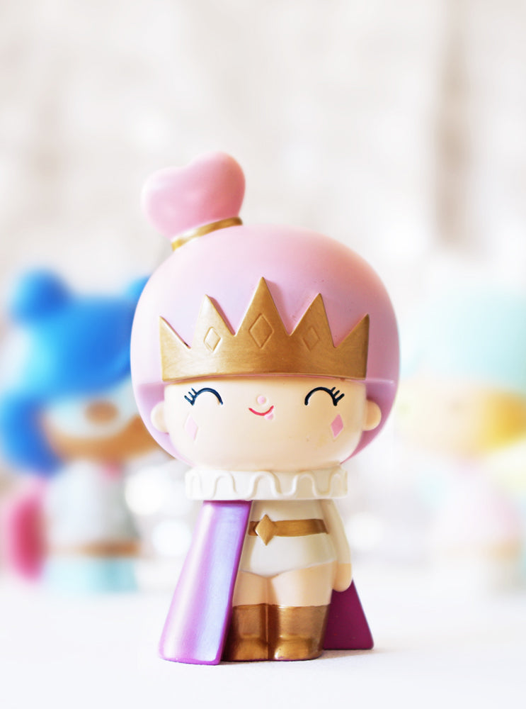 Fabulous You Momiji doll with a pink crown, cape, and cheerful smile, posed before softly blurred colorful figures. — Momiji doll