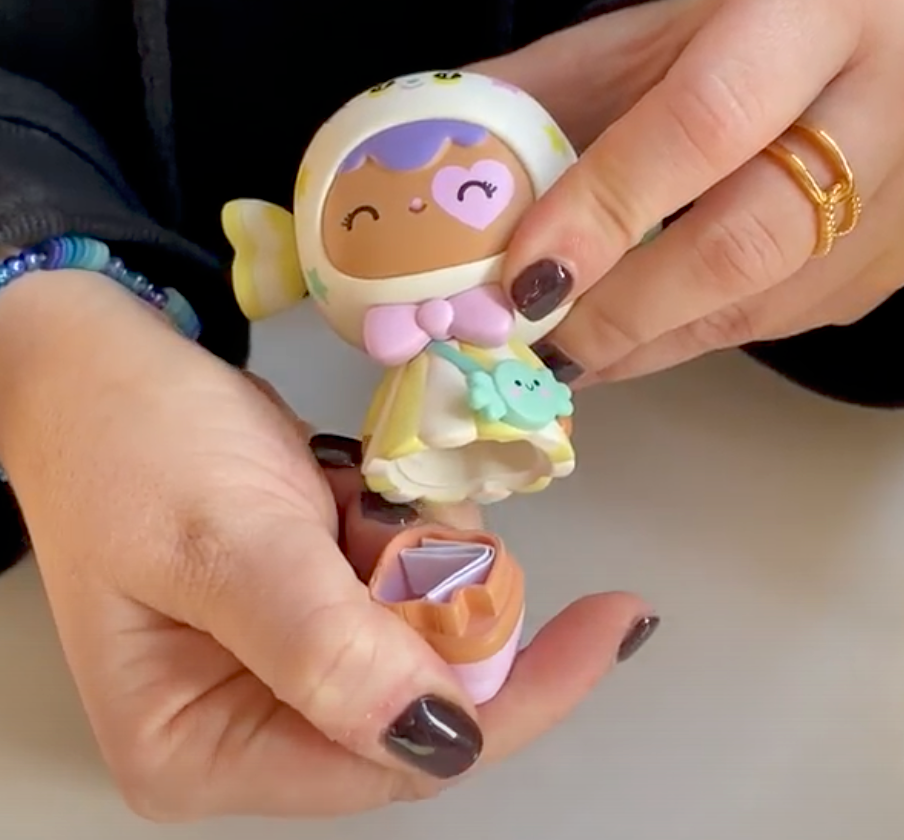 Someone holds a Candy Button Momiji doll, 8cm tall, vinyl with pastel colors. Removable base hides a tiny folded wishing paper inside. — Momiji doll