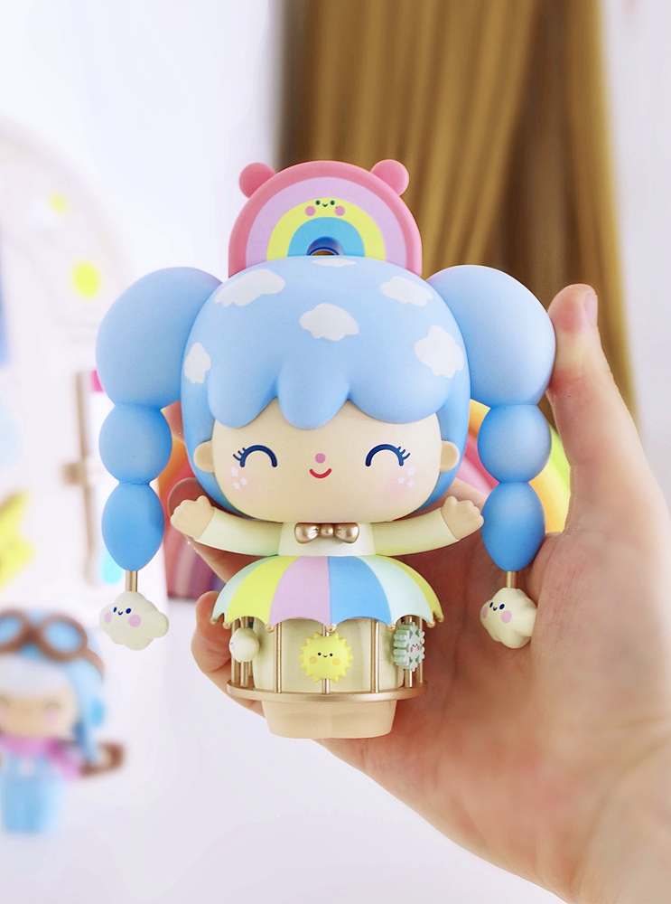 A hand holds a Momiji doll named Sky Dreamer, with blue pigtails, rainbow accents, clouds, and playful animal details. — Momiji doll